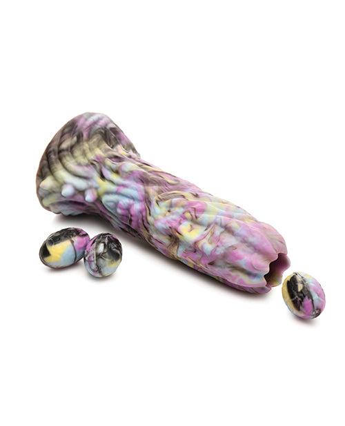 The Creature Cocks Dragon Spawn Ovipositor with Eggs lays flat on the ground with an egg "popping out" of the top of the dildo, showcasing how the toy works. | Kinkly Shop