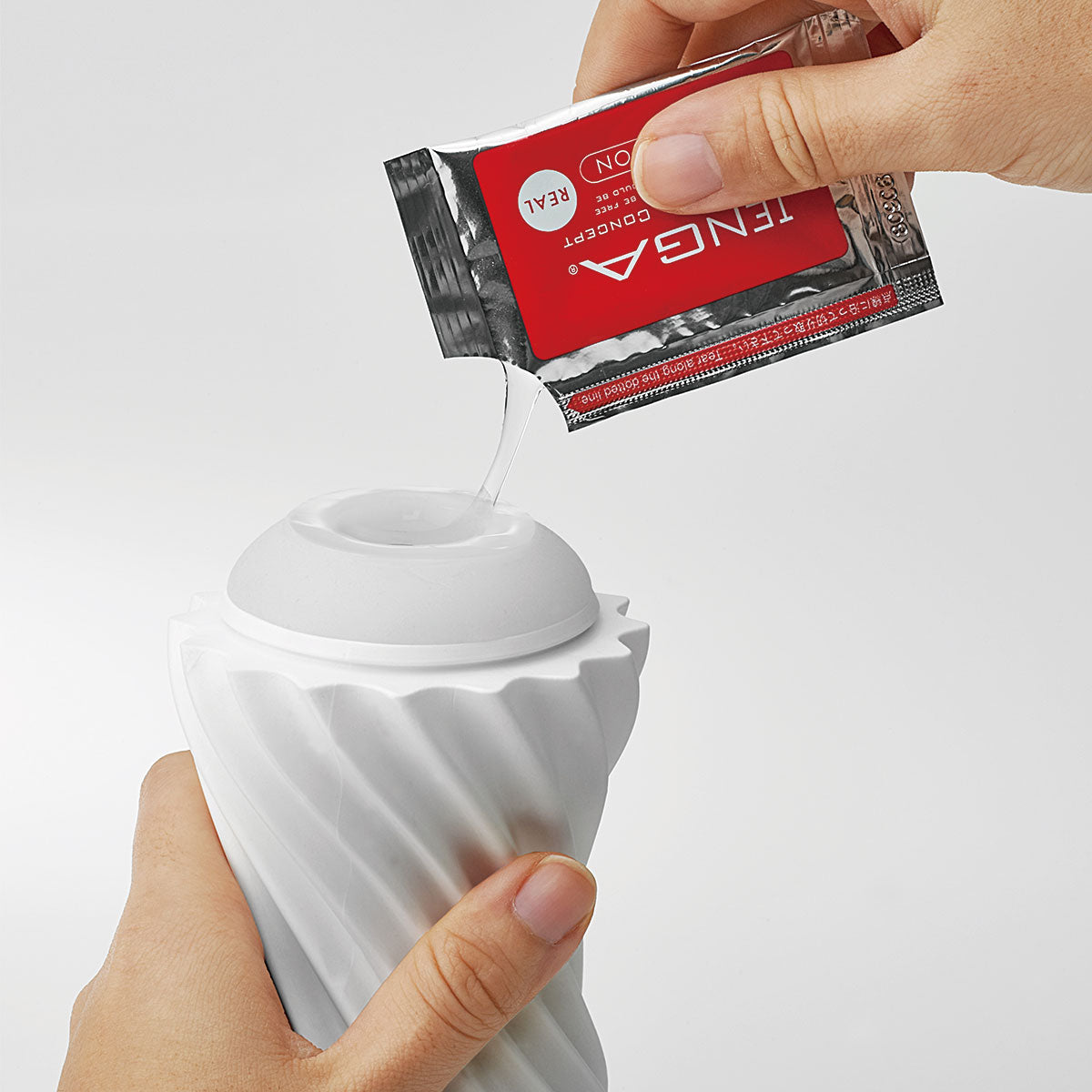 A hand pours some of the included, sample-size of TENGA Real lube onto the entrance of the TENGA Flex. One sample packet is included. | Kinkly Shop