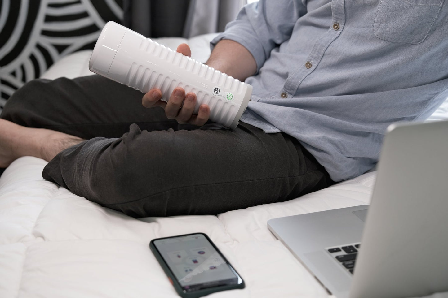 A person holds the Lovense Max 2 while looking at their cell phone and their laptop. The stroker is about twice the length of their gripping hand. | Kinkly Shop