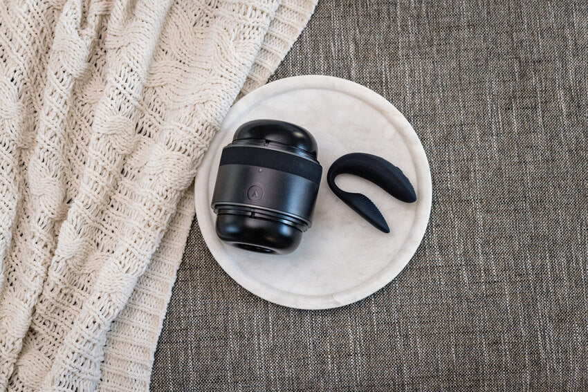 The Arcwave Voy and the We-Vibe Sync that's included in the Arcwave Double the Fun kit sitting out on top of a round dish that sits on a couch. | Kinkly Shop