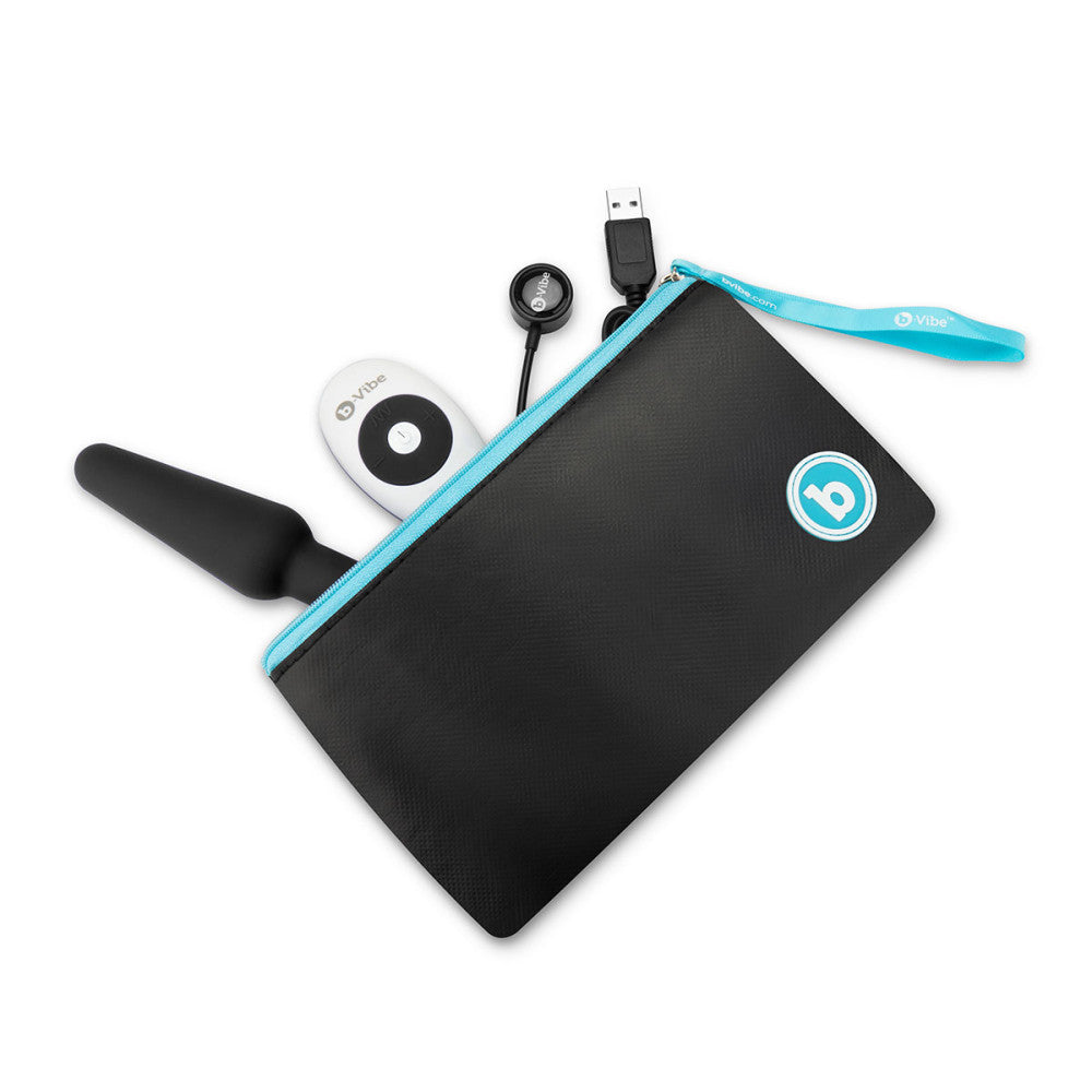 The carrying pouch for the b-Vibe Remote Trio Plug, unzipped and laying on its side. The plug itself, the remote, and the charging cable are peeking out from the pouch. The pouch is large enough that a bottle of lube could fit with the toy. | Kinkly Shop