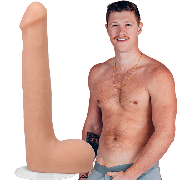 A shirtless Oliver Flynn looks into the camera while grabbing his crotch. The Signature Cocks - Oliver Flynn dildo is shown next to the porn star. The dildo was modeled directly from him. | Kinkly Shop