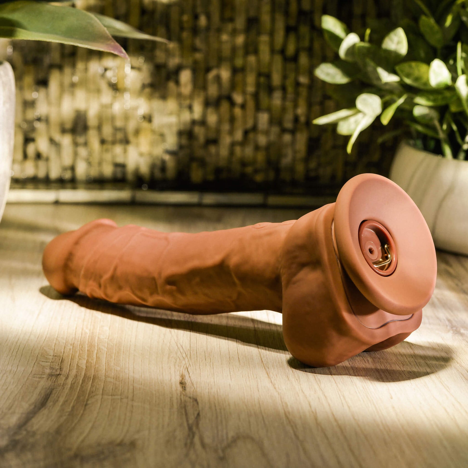 Close-up of the Evolved Big Shot Vibrating Squirting Dildo in Espresso in a spa. There's a spotlight on top of the toy, making it easy to view all of the toy's intense veined texturing. This angle showcases how the ejaculation chamber is recessed into the concave suction cup base to allow the toy to have a suction cup base while simultaneously offering access to fill the chamber. | Kinkly Shop