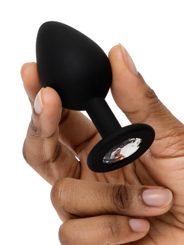 A hand holds the butt plug that comes in the Fifty Shades of Grey Come to Bed Kit. It looks like it is about the width of two of the person's fingers, and it is about the length of one of their fingers. | Kinkly Shop