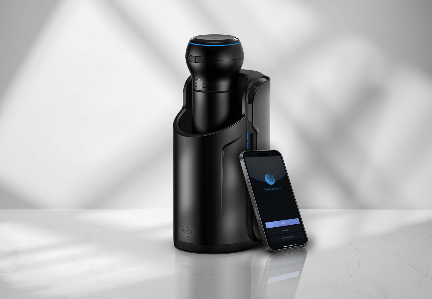 The KIIROO Power Blow attached to the top of a stroker that's been slid inside of the KIIROO KEON. A cell phone, open to the free cell phone app, leans up against the KEON. | Kinkly Shop
