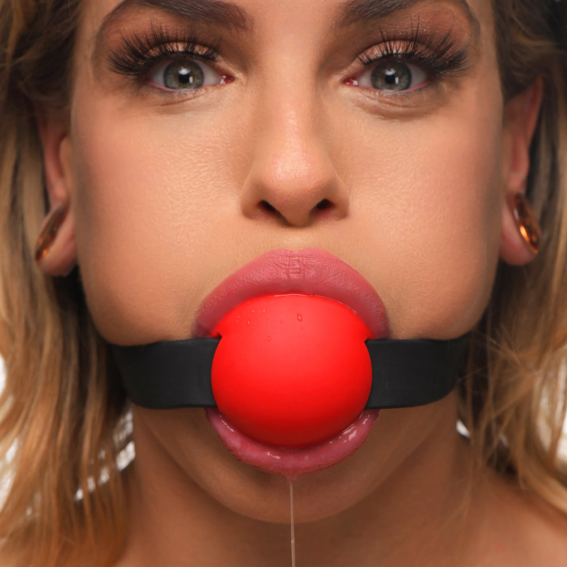 A person wears the Master Series Gag Order, looking straight into the camera. The gag looks like a ball gag from a viewer's perspective. | Kinkly Shop
