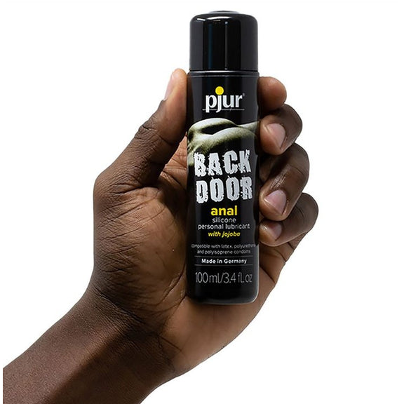 A hand holds a bottle of the Pjur Back Door Anal Silicone-Based in 100ml size. It's a somewhat slender bottle, and it looks like it's shorter than the palm of this person's hand. | Kinkly Shop