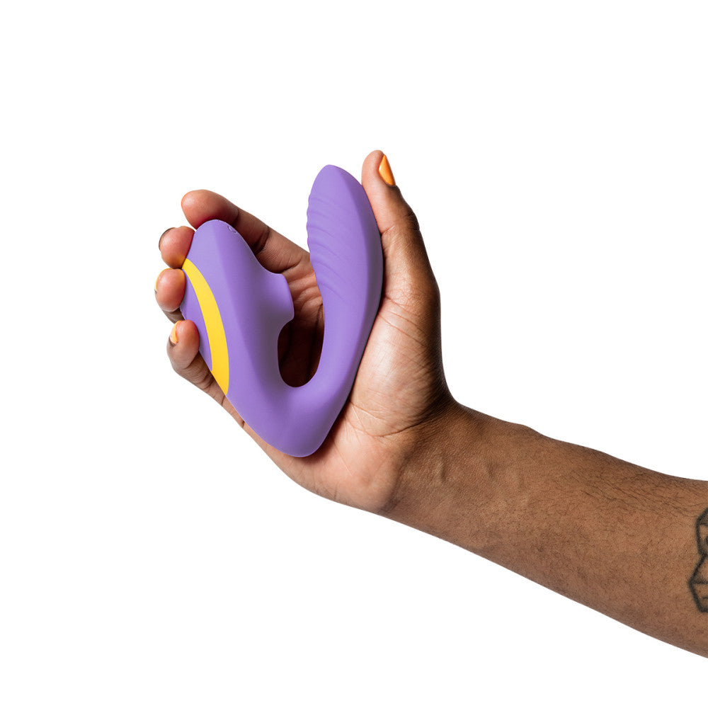 A hand holds the ROMP Reverb up against a white background. The hand is squeezing both sides of the Reverb at the same time, causing the clitoral air suction end to nearly touch the insertable end to showcase how flexible the joint of the toy is. | Kinkly Shop