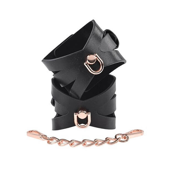 The two Sportsheets Brat Cuffs are fastened together into their cuff-like shape and stacked on top of one another. The rose gold hardware matches the rose gold hardware of the included chain. The cuffs look very unique and fashion-forward. | Kinkly Shop