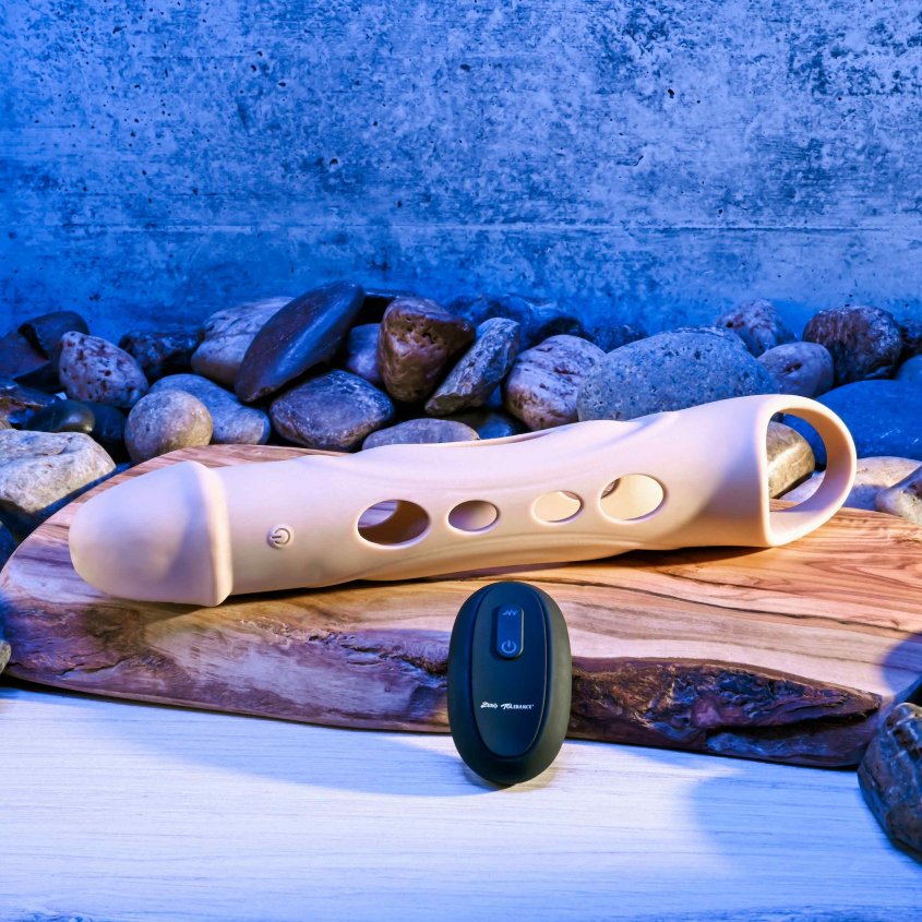 The Evolved Big Shaft Extender in Cream sitting on a plank of wood with the remote control sitting in front of it. The Evolved Big Shaft Extender itself has a single Power button built into the shaft of the toy. The remote control has two buttons on it. | Kinkly Shop