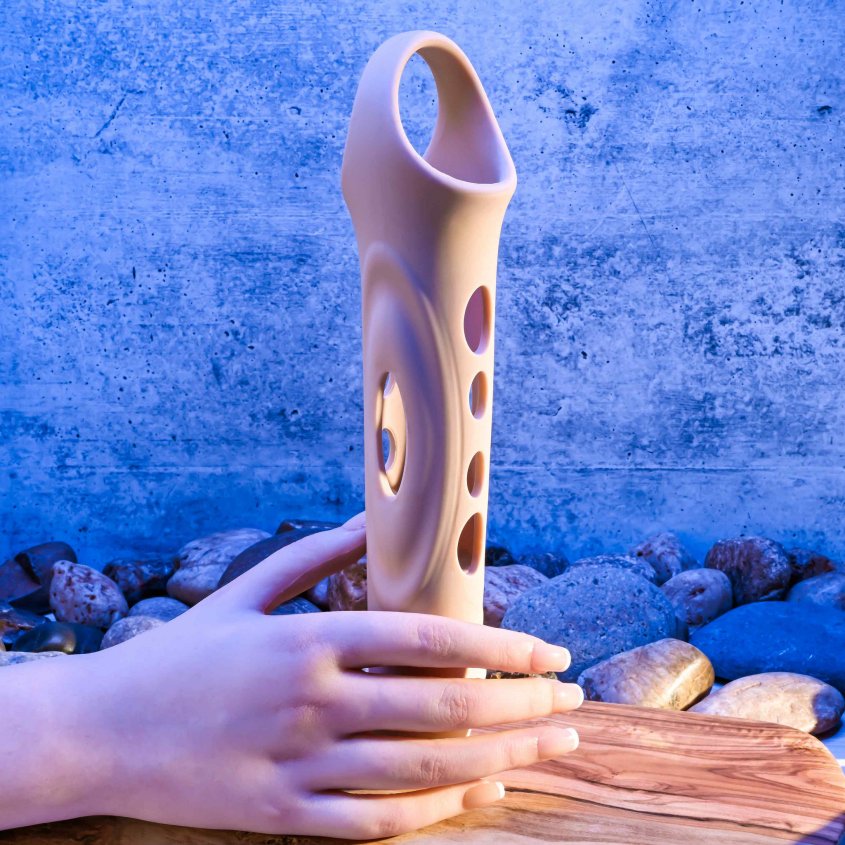 A mannequin hand holds the Evolved Big Shaft Extender. Without anything inside of the extender, it's possible to see through the extender to the background behind it. | Kinkly Shop