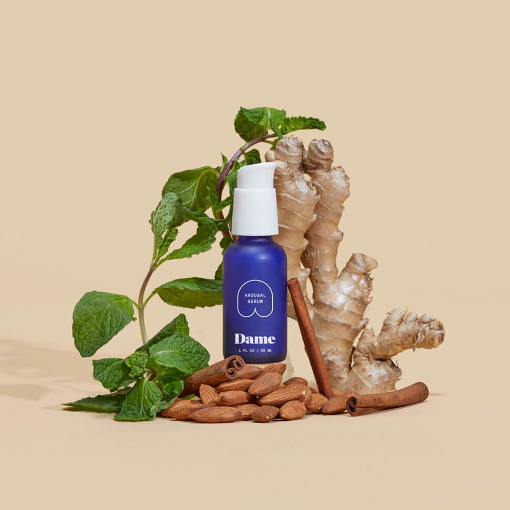 The Dame Arousal Serum bottle sits in a pile of different items that make up the ingredients of their formula. | Kinkly Shop