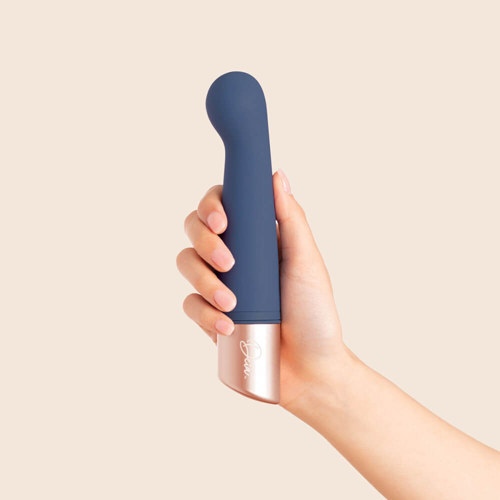 A person's hand is gripping onto the Deia The Couple interchangeable tip vibrator in front of a brown background. It looks like their fingers could wrap all the way around the base of the vibrator if they tried to. | Kinkly Shop