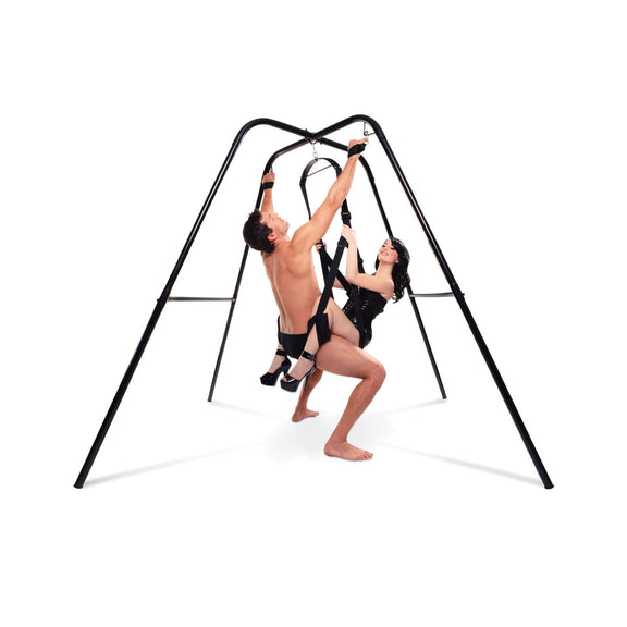 Two people are using a sex swing that's hanging from the Fetish Fantasy Series Sex Swing Stand. The person sitting on top of the sex swing also has their hands bound up above their head using the bondage loops built into the frame. | Kinkly Shop