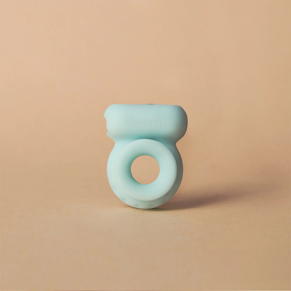 The OhNut Vibrating Ring against a brown background. This view showcases the long, horizontal positioning of the vibrator up against the OhNut ring. It doesn't protrude too far away from the ring; instead, it runs horizontally alongside the ring. | Kinkly Shop