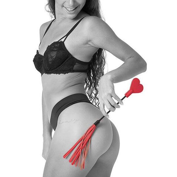 A person in lingerie holds the Sportsheets Amor Crop up against their butt. The tails of the flogger end droop slightly. The Sportsheets Amor Crop looks short and portable. | Kinkly Shop