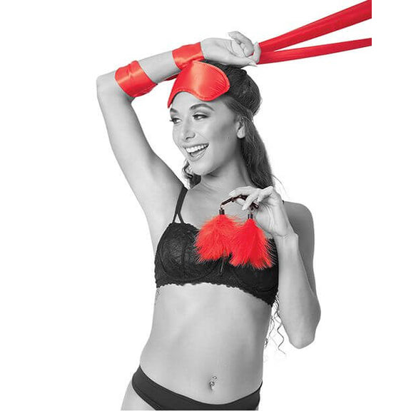 A person is smiling and laughing as they wear the red blindfold, have the red satin sash wrapped around their wrists, and holding the two feathered nipple clamps in their hands. | Kinkly Shop