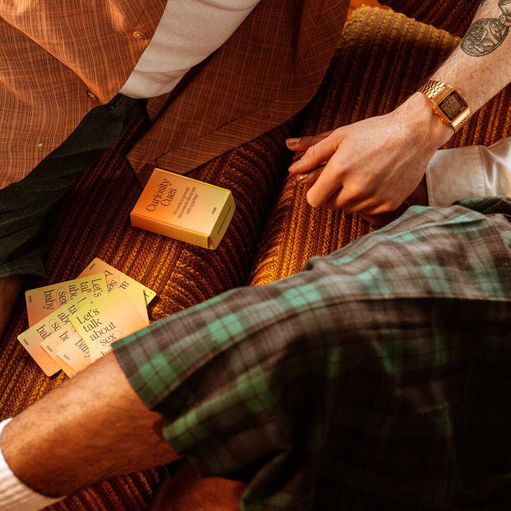 A couple is holding hands while sitting on the couch. The cards are spread out on the surface of the couch between the couple. | Kinkly Shop