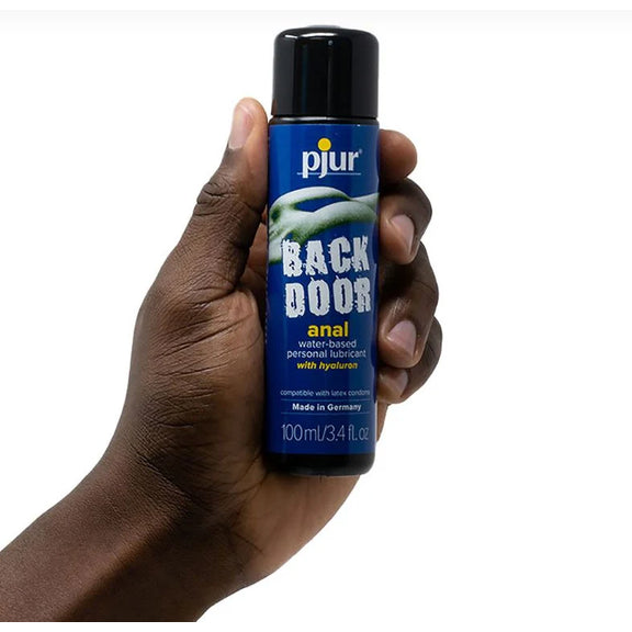 A hand holds the Pjur Back Door Water-Based 100ml bottle of the lube. It looks like a standard-sized bottle in their hand. | Kinkly