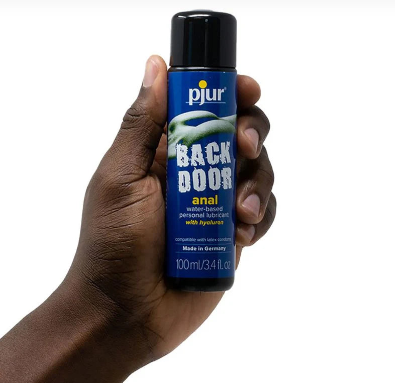 A hand holds the Pjur Back Door Water-Based 100ml bottle of the lube. It looks like a standard-sized bottle in their hand. | Kinkly
