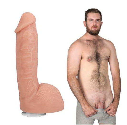 A shirtless Girthmasterr stands while looking at the camera. The Signature Cocks - Girthmasterr dildo, modeled after their penis, is shown next to them. | Kinkly Shop
