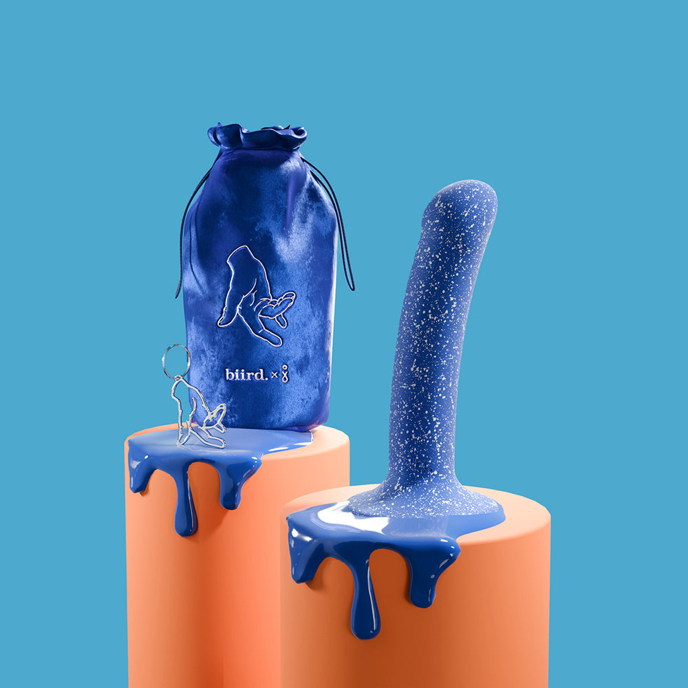 The Biird Bae sits out on an orange pedestal. The toy's bag and a keychain charm are next to it. Both pedestals are dripping in matching blue paint. | Kinkly Shop