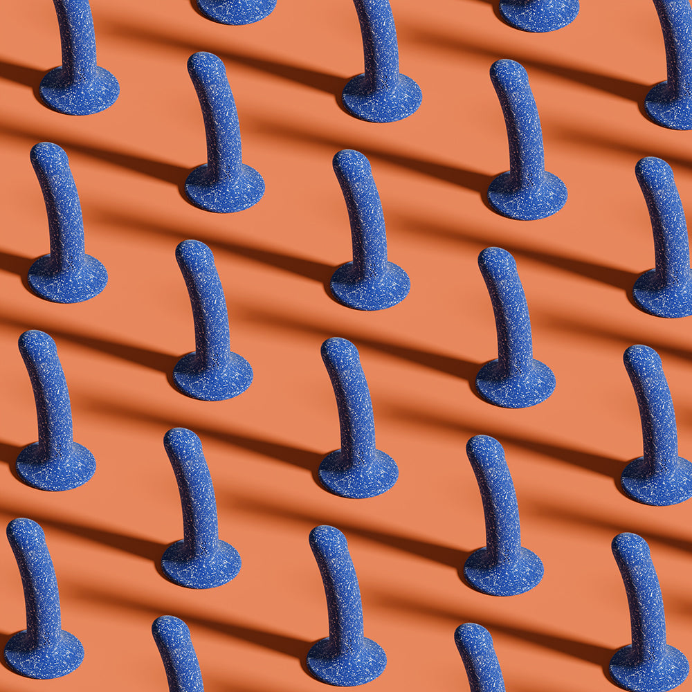 An entire army of Biird Bae sitting upright on an orange background. A strong light source from the lower right corner of the image is causing each one of the dildos to cast a very long shadow across the orange background. It's very artsy. | Kinkly Shop