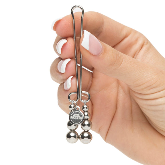 A hand holds the Fifty Shades "Just Sensation" Clitoral Clamp. It looks light and delicate in their fingers. The charms on the end look particularly erotic. | Kinkly Shop