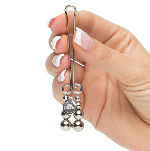 A hand holds the Fifty Shades "Just Sensation" Clitoral Clamp. It looks light and delicate in their fingers. The charms on the end look particularly erotic. | Kinkly Shop