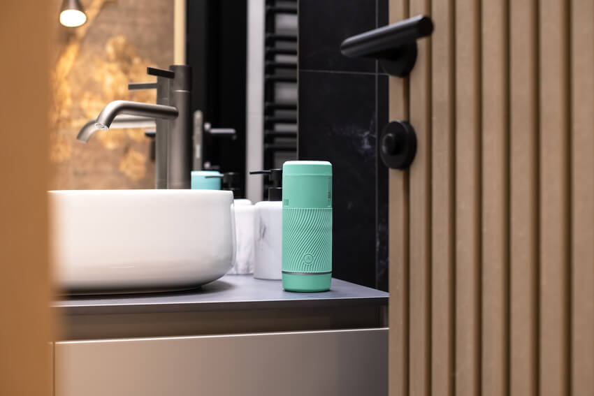 The Arcwave Pow in Mint sitting out next to a ledge of a kitchen sink. It looks like a Bluetooth speaker. | Kinkly Shop