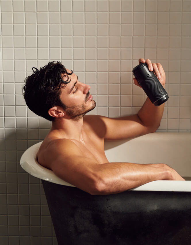 A person sitting in a bathtub smiles at the Arcwave Pow they are holding. The Pow is waterproof. | Kinkly Shop