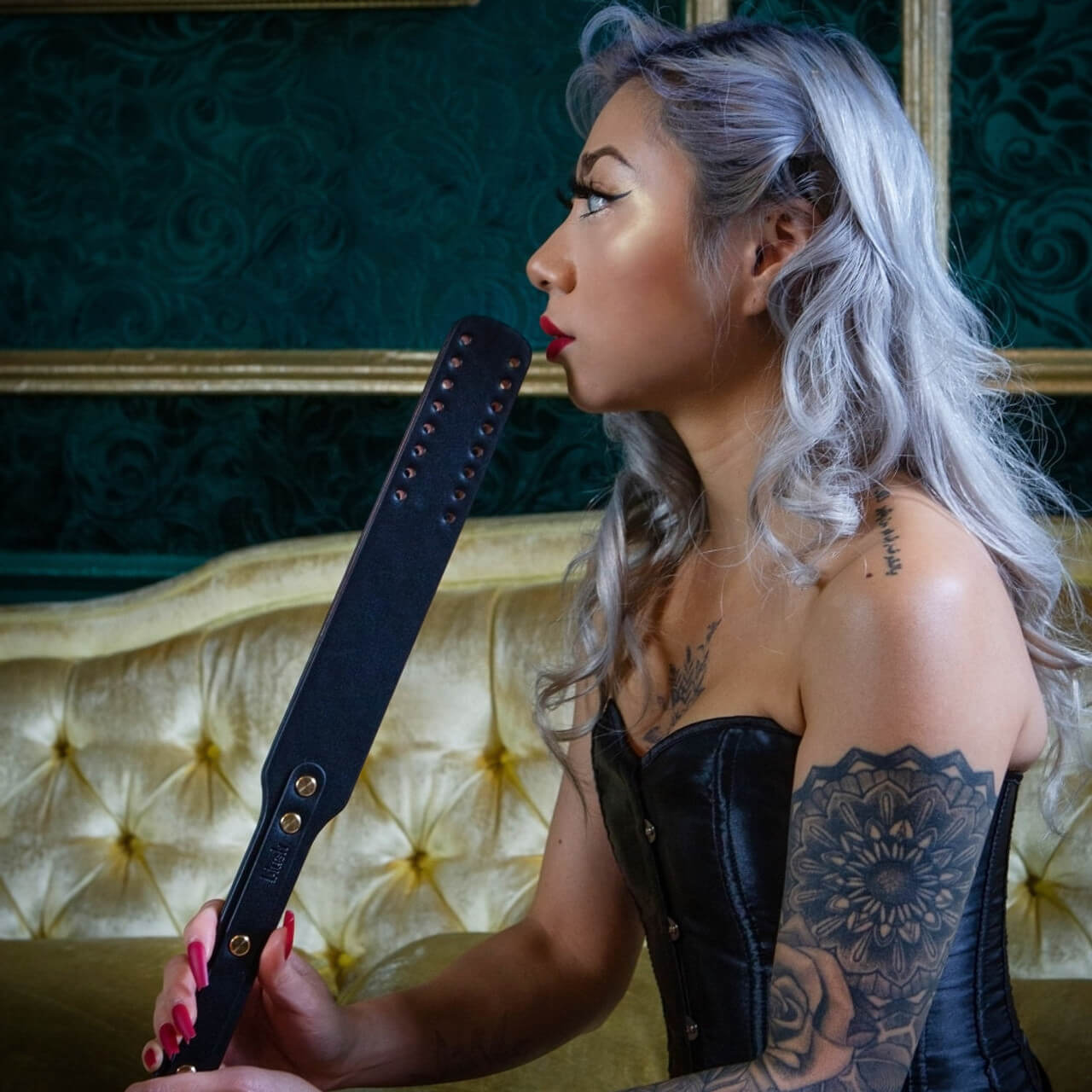 A person sitting on a couch is holding the paddle included in the Blush Temptasia Safe Word Bondage Kit. | Kinkly Shop