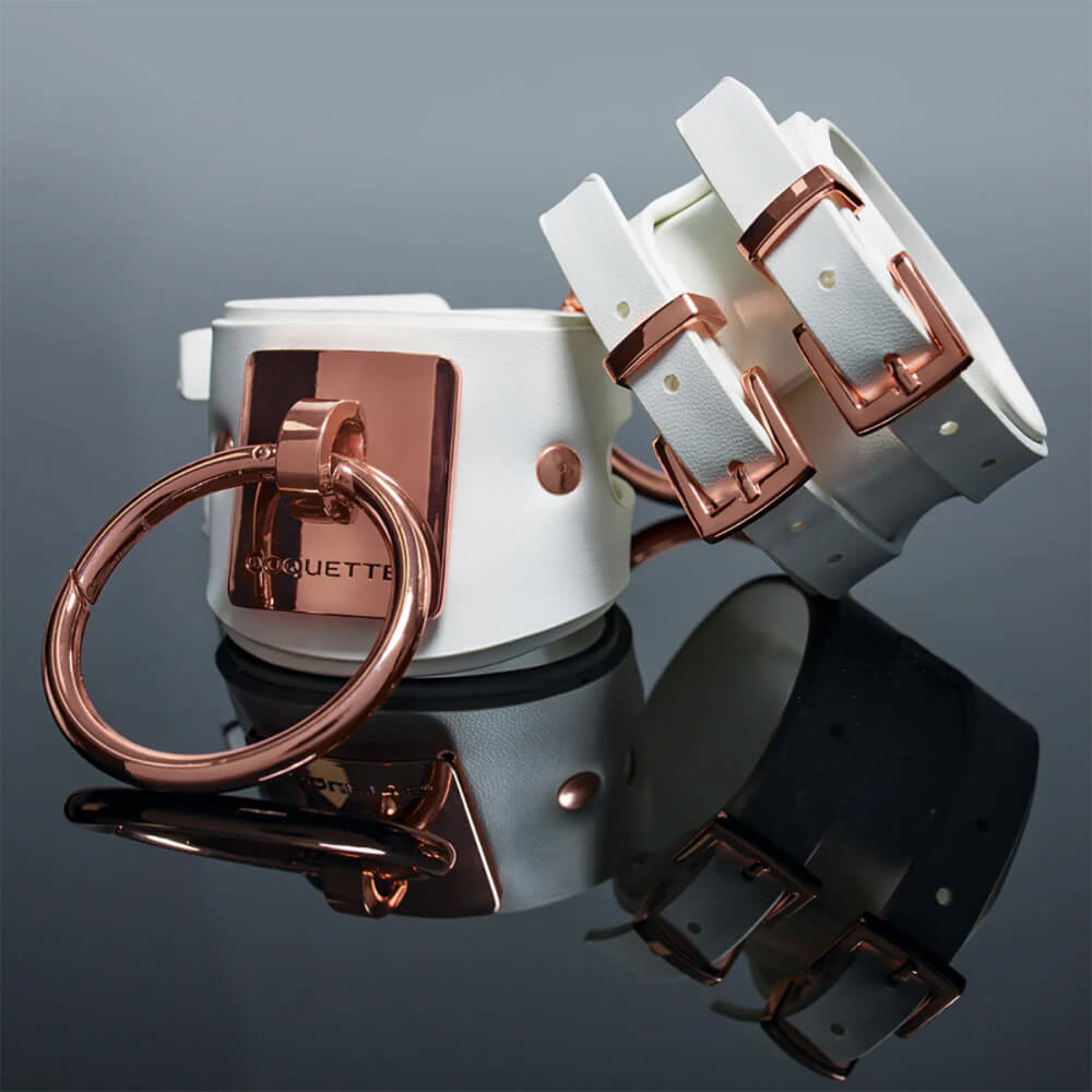 Close-up of the Coquette White and Rose Gold Adjustable Cuffs and their backside. The high-quality leather grain can be seen from this close-up, and it also showcases the double-strap design of the fastening straps on the cuffs. | Kinkly Shop