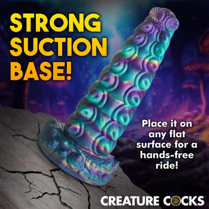 The Creature Cocks Chrysalis shown stuck onto a cracked rock that would not actually support a suction cup if this was real. Text on the image reads: "Strong suction base. Place it on any flat surface for a hands-free ride." | Kinkly Shop