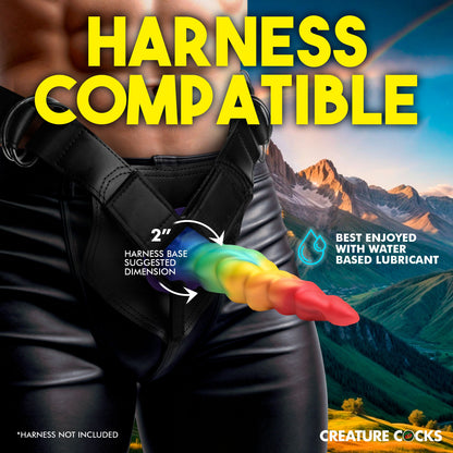 A person wears the Creature Cocks Magic Rider in a strap-on harness. Text on the image reads: Harness compatible. 2" harness base suggested dimension. Best enjoyed with water-based lube. Harness is not included. | Kinkly Shop
