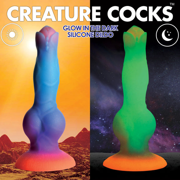 Two images of the Creature Cocks Space Cock shown side-by-side. In one, the dildo is shown in daylight with orange, purple, and blue hues. In the shot next to it, it's shown in the dark with the glow-in-the-dark green and orange at the base. | Kinkly Shop