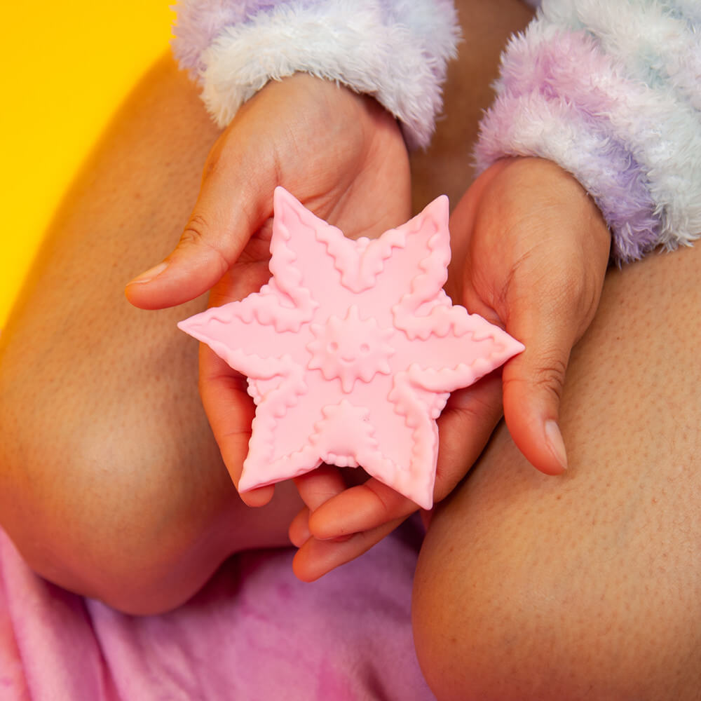Two hands hold the Cute Little Fuckers Starsi in front of bare thighs. The vibrator is a wide, star-shaped toy that fits into two hands, cradled together, perfectly. The texturing and design is very detailed. | Kinkly Shop
