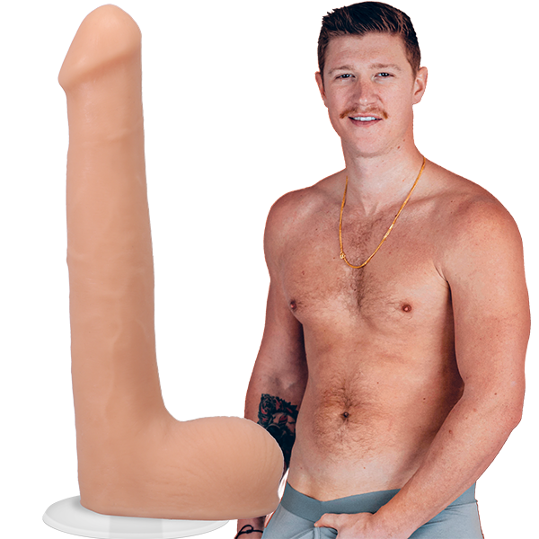 A shirtless Oliver Flynn looks into the camera while grabbing his crotch. The Signature Cocks - Oliver Flynn dildo is shown next to the porn star. The dildo was modeled directly from him. | Kinkly Shop