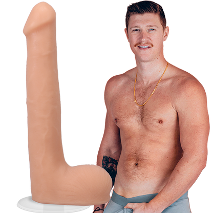 A shirtless Oliver Flynn looks into the camera while grabbing his crotch. The Signature Cocks - Oliver Flynn dildo is shown next to the porn star. The dildo was modeled directly from him. | Kinkly Shop