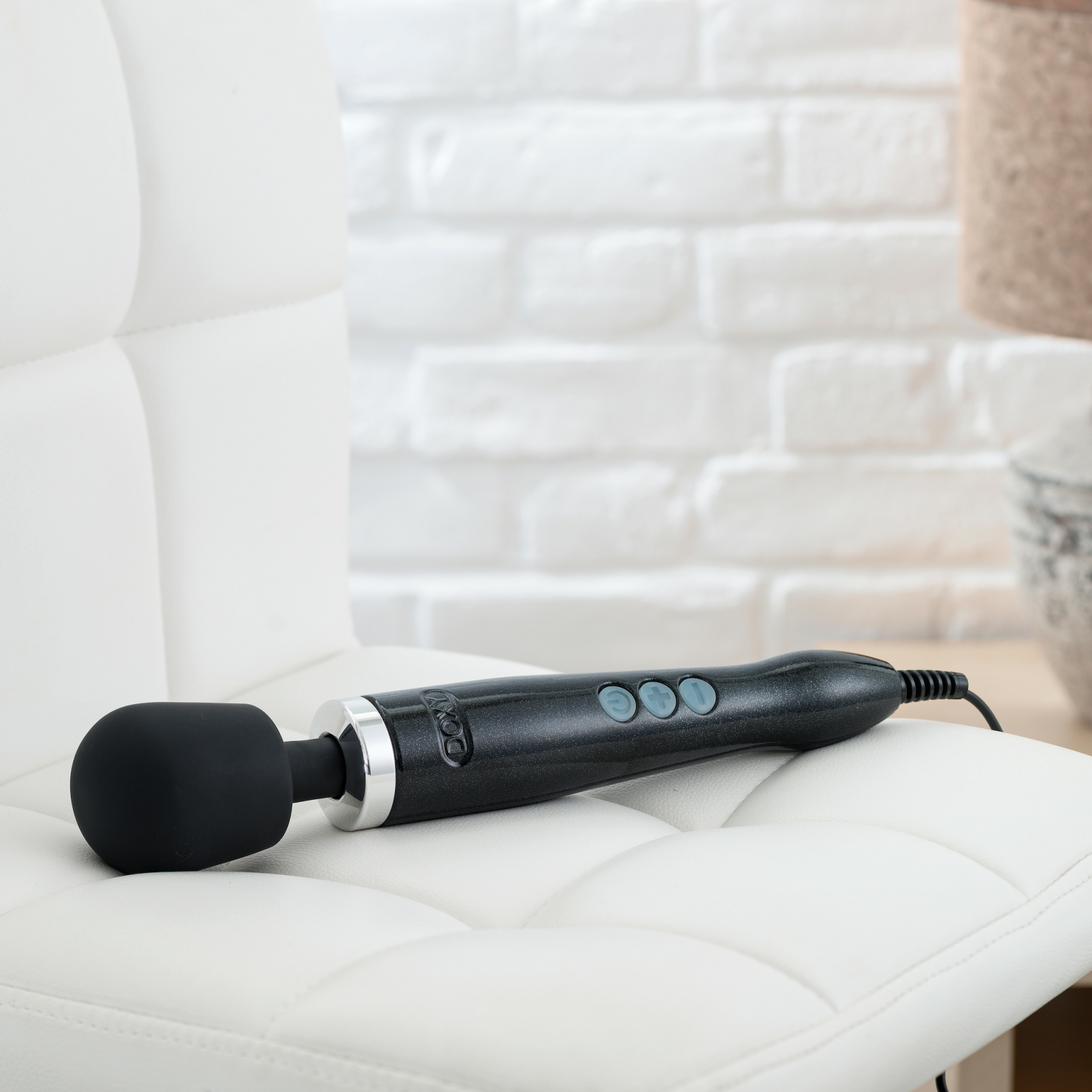 The Doxy Die Cast rests on top of a chair. It takes up most of the width of the chair, and the power cable, which cannot be removed, hangs off the edge of the seat. | Kinkly Shop