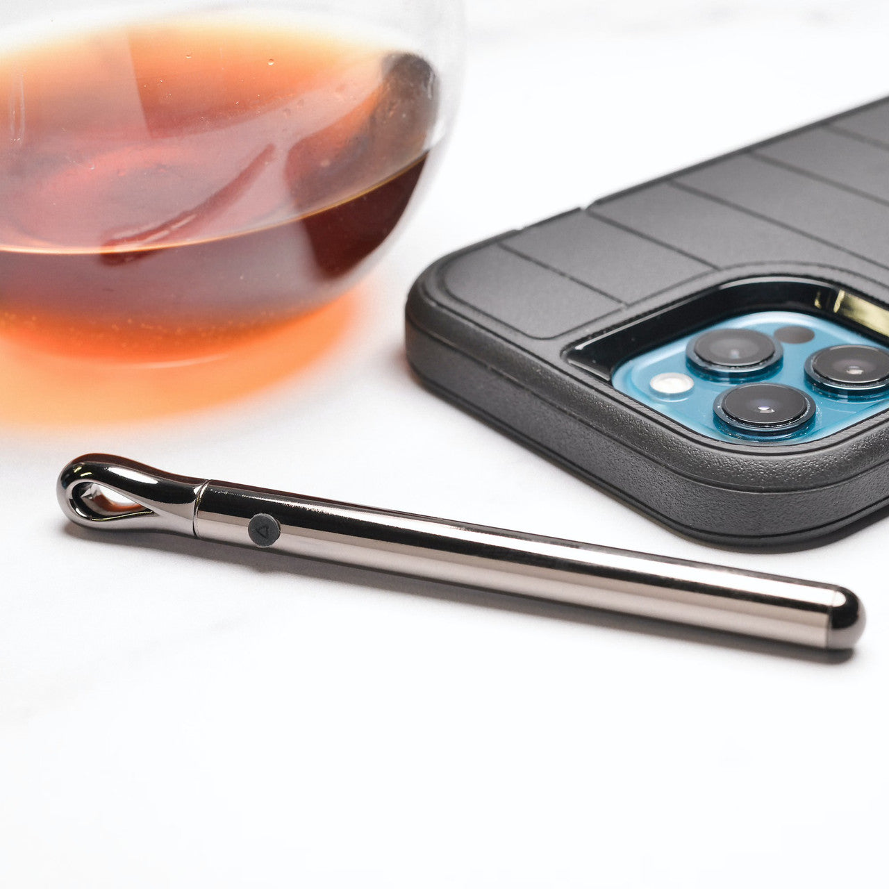 The Evolved Pen Pal sits out in front of a glass of brown liquid and a cell phone. It looks like a small pen laying out on a table. | Kinkly