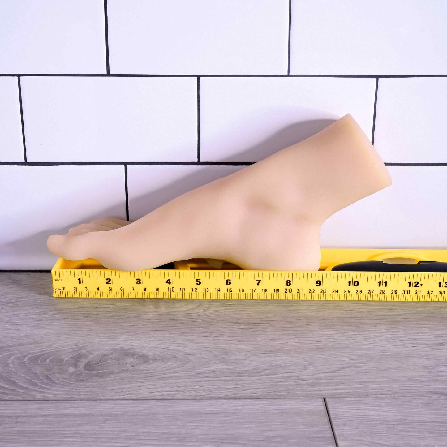 The Evolved Pussy Footin' up against a wall next to a yellow measuring tape. The sole of the foot is 9" in total length. | Kinkly Shop