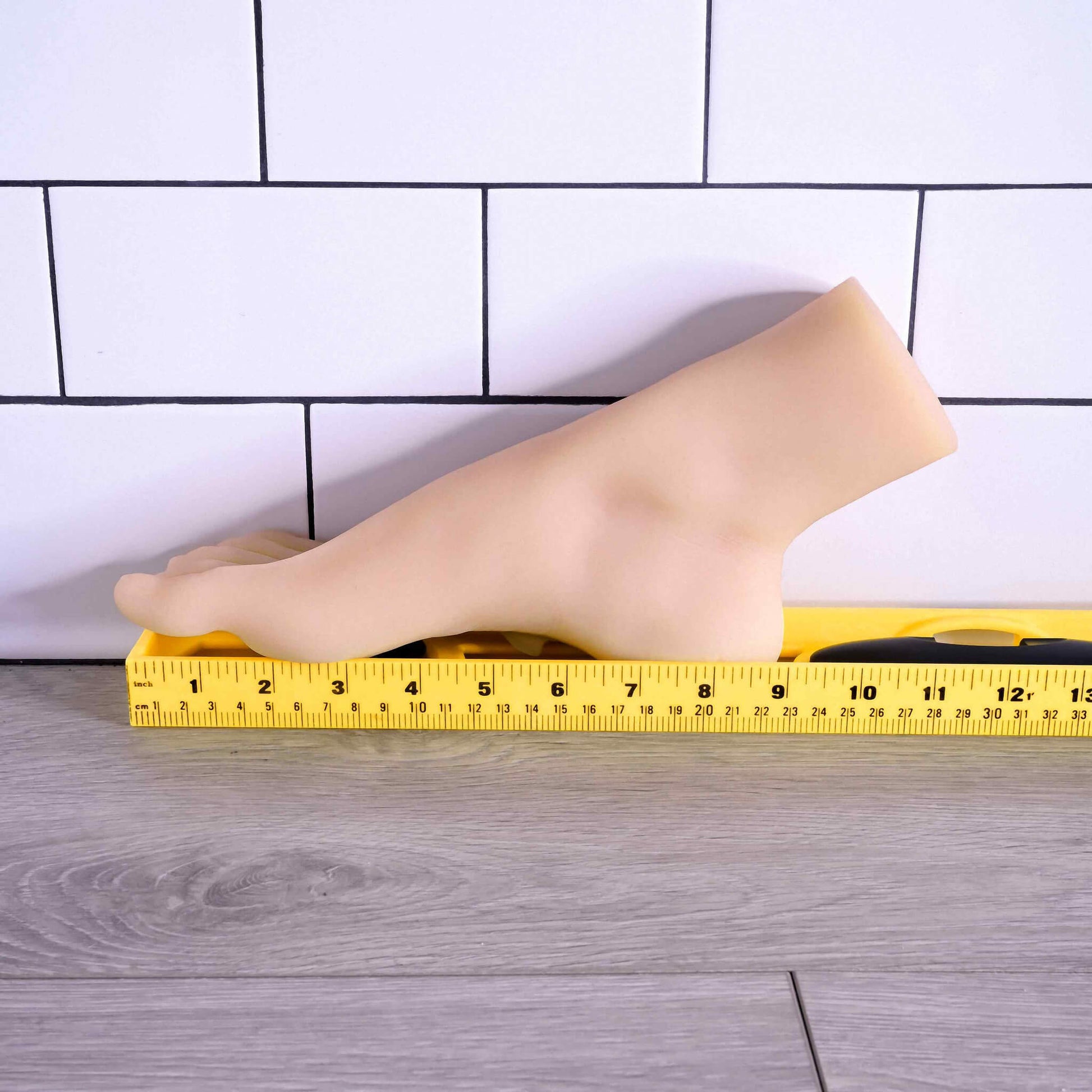 The Evolved Pussy Footin' up against a wall next to a yellow measuring tape. The sole of the foot is 9" in total length. | Kinkly Shop