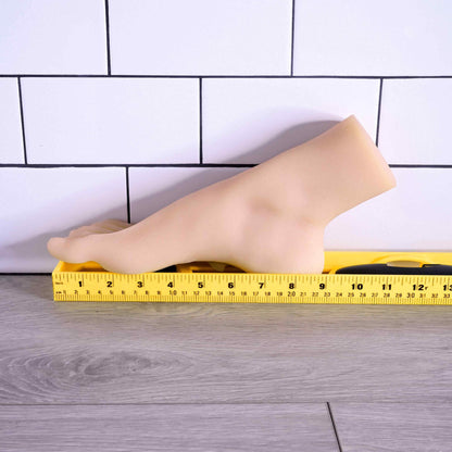 The Evolved Pussy Footin' up against a wall next to a yellow measuring tape. The sole of the foot is 9" in total length. | Kinkly Shop