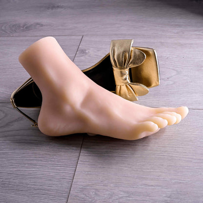 The Evolved Pussy Footin' in Cream laying out next to a gold high heeled shoe. It looks very realistic and is a life-sized foot that could fit within the shoe. | Kinkly Shop