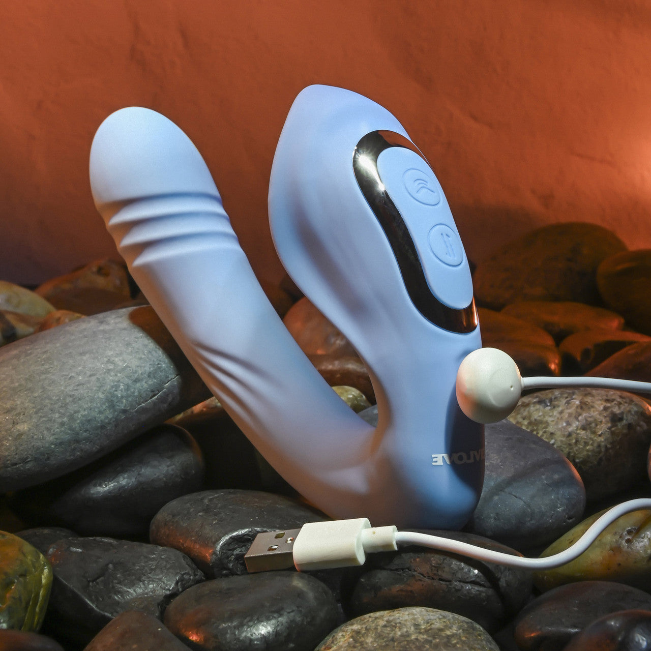 The Evolved Tap & Thrust shown attached to the charging cable that charges it. The charger is a magnetic charger with charging prongs on the front of the vibrator near the two control buttons | Kinkly Shop