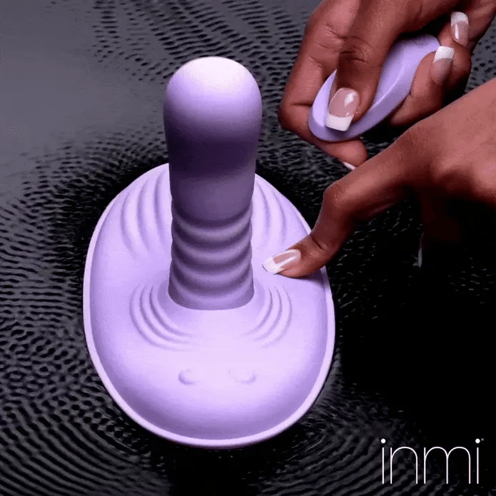 GIF shows the thrusting shaft of the Inmi Thrust N' Grind as the sex toy sits on a flat surface. A person holds the remote and controls the toy from nearby. | Kinkly Shop