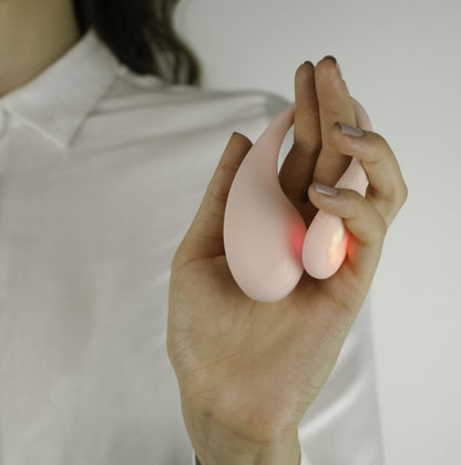 A person holds the KIIROO Spot in their hands. The LED lights on the tail of the Spot give off a gentle red glow against the toy's body and the person's fingers. | Kinkly Shop