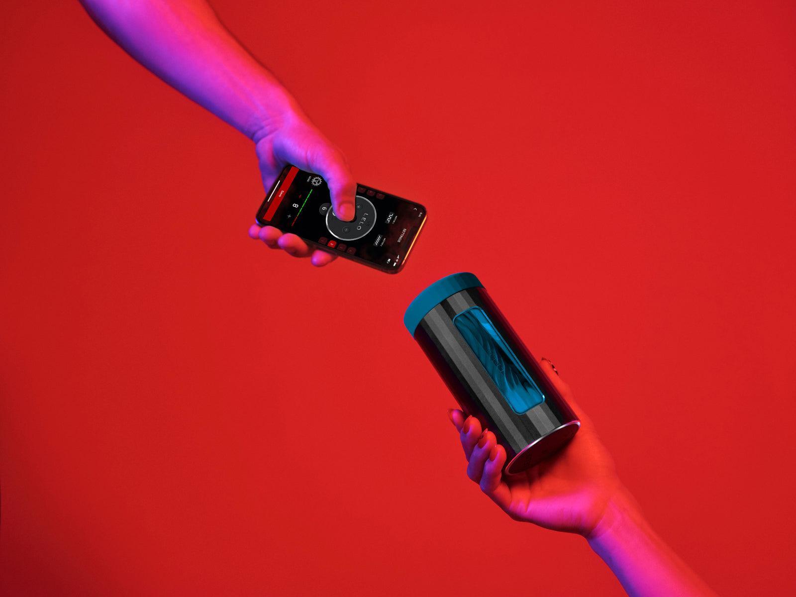 Two hands against a red background. One holds a LELO F1S V3 while another holds a cell phone, open to the LELO app to control the stroker. | Kinkly Shop