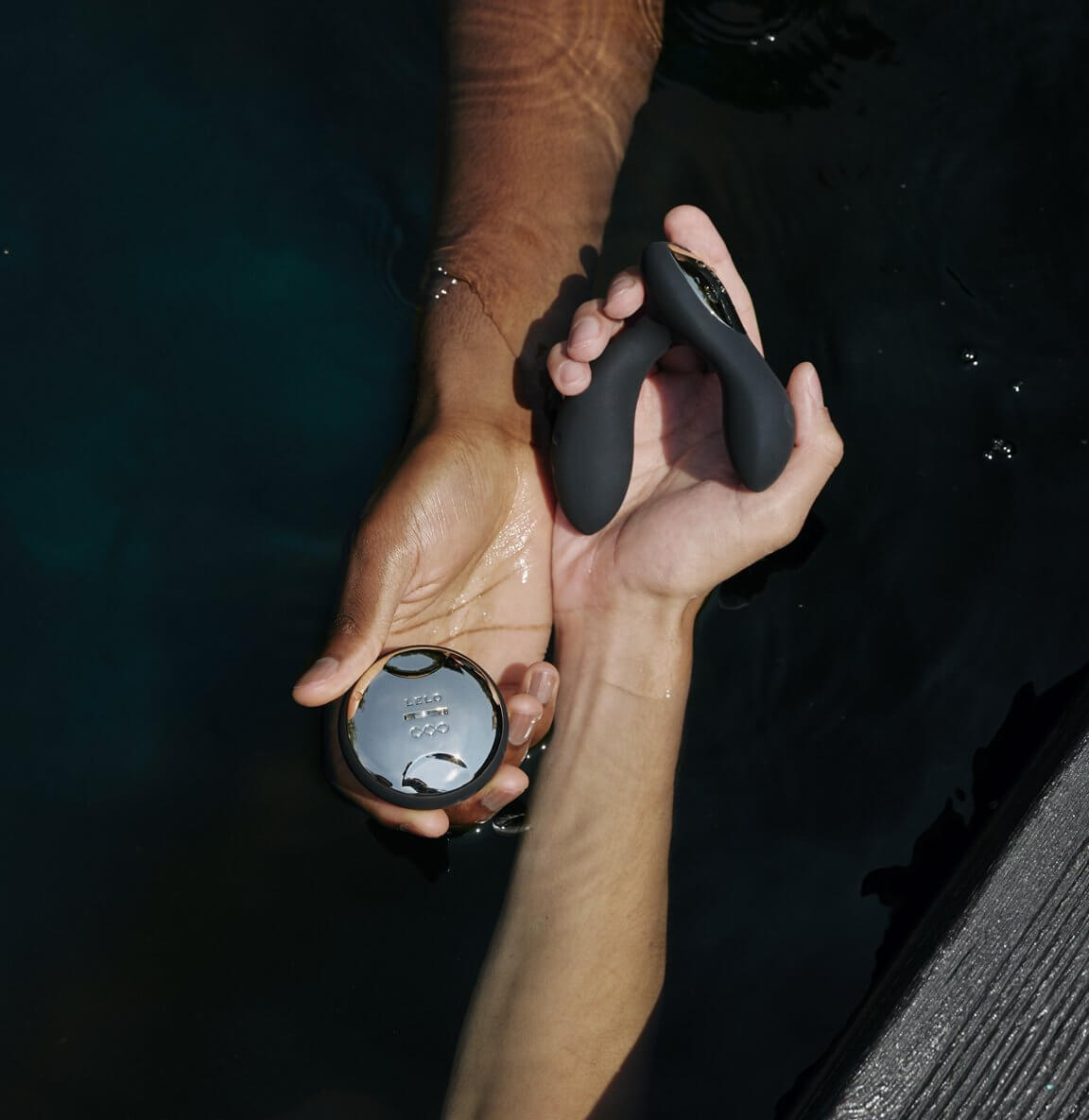 Two hands hold the LELO HUGO 2 and remote above a body of water. The prostate massager fits comfortably within the holder's hand, and the insertable shaft looks like it's about the size of two fingers. The remote control fits comfortably into the person's palm. | Kinkly Shop